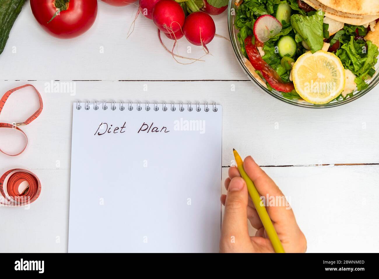 Frau Hand halten Stift und schreiben Worte Diät-Plan in einem Notizblock auf weißem Holztisch mit einer Schüssel Salat und Gemüse Stockfoto