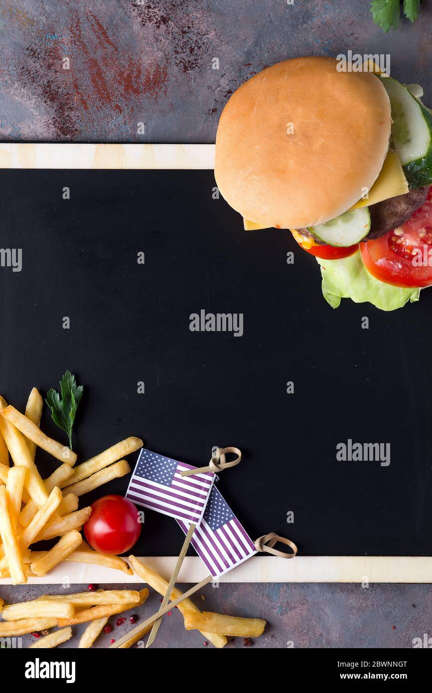 Leckere gegrillte hausgemachte Burger Kochen mit Rindfleisch, Tomaten, Käse, Gurke und Salat auf einer Kreidetafel mit Pommes Frites und der US-Flagge Stockfoto