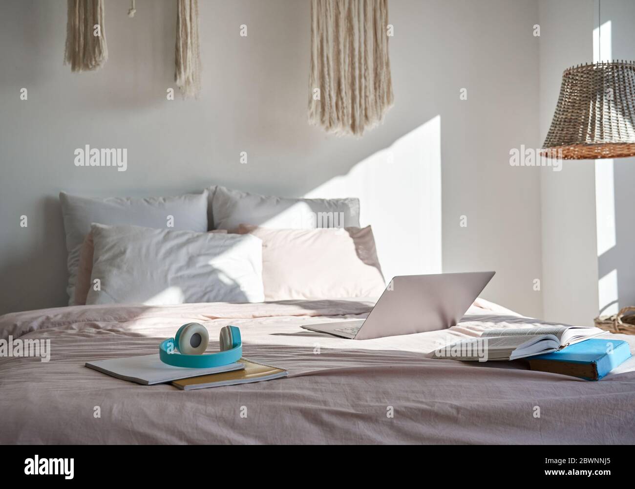 Moderne gemütliche Hygge Schlafzimmer mit Laptop, Kopfhörer, Bücher auf einem gemütlichen Bett. Stockfoto