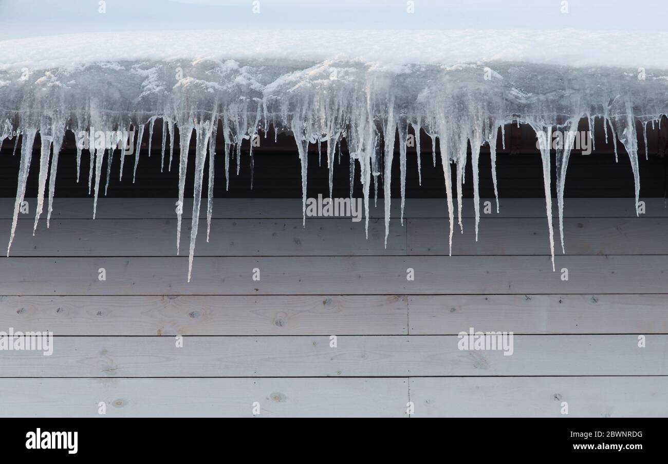 Gebäude mit Eiszapfen bedeckt, Nahaufnahme. Eis Stalaktit hängt vom Dach, Kopie Raum. Schlechte Wärmedämmung des Daches führt zur Bildung von ic Stockfoto
