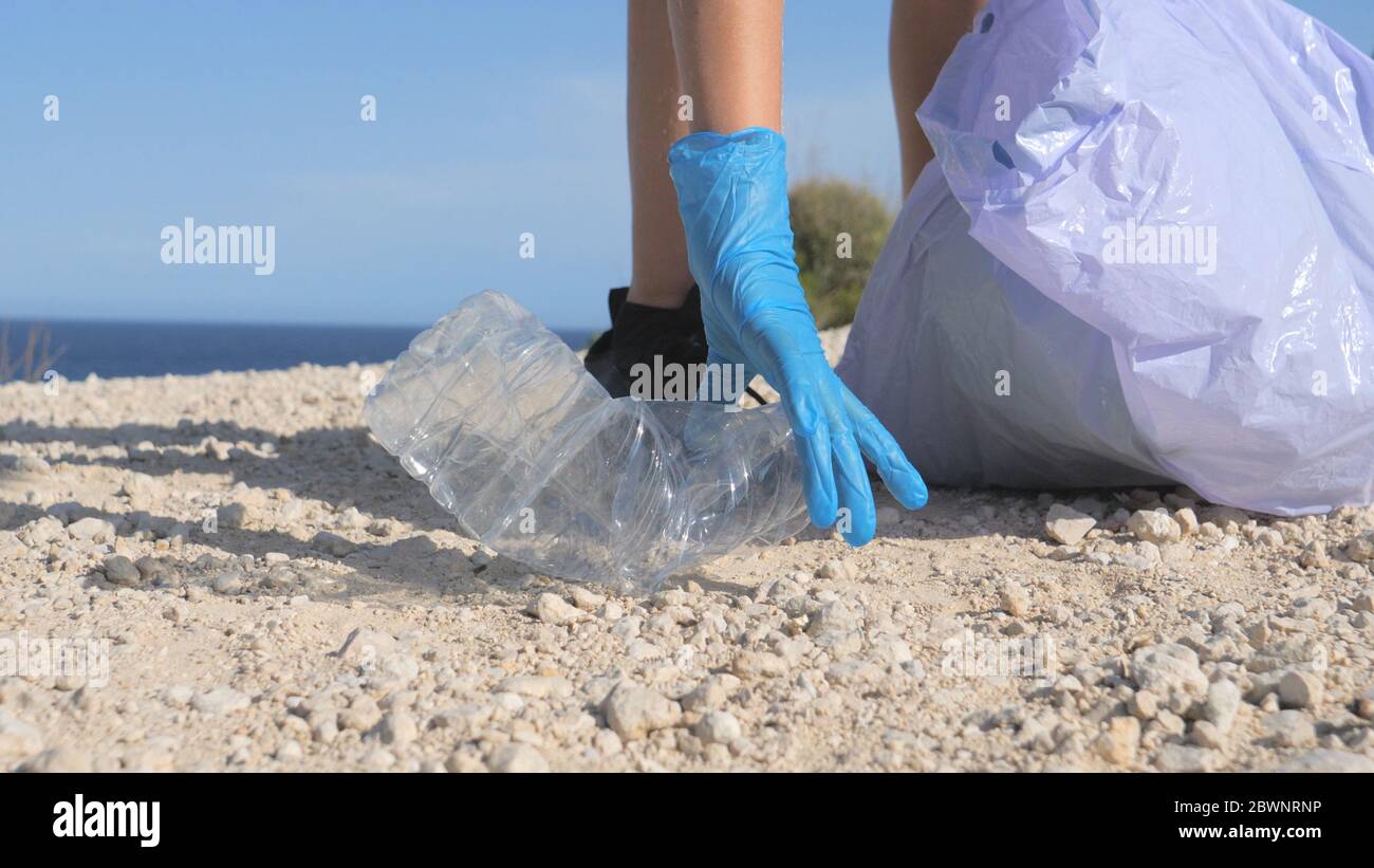 Freiwillige Hand mit Schutzhandschuh Reinigung Strand aus Kunststoff. Frau nimmt Plastikflaschen Abfall und setzen in Plastiktüte für Recycling Stockfoto