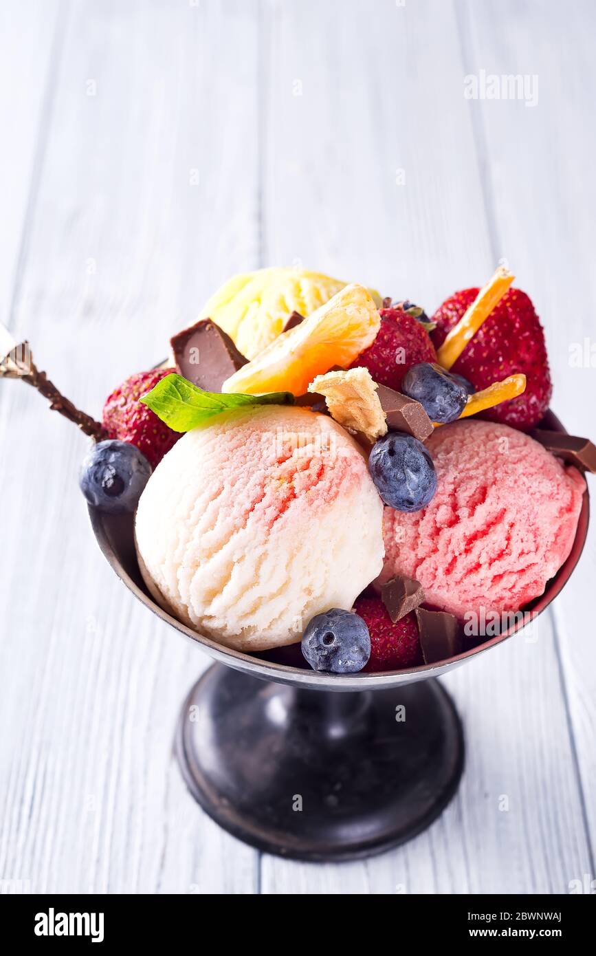 Trio aus leckeren Zitrone, Vanille und Erdbeere aromatisiert gefrorenes Dessert-Eis in einer Metallschüssel mit Beeren auf Holz Stockfoto
