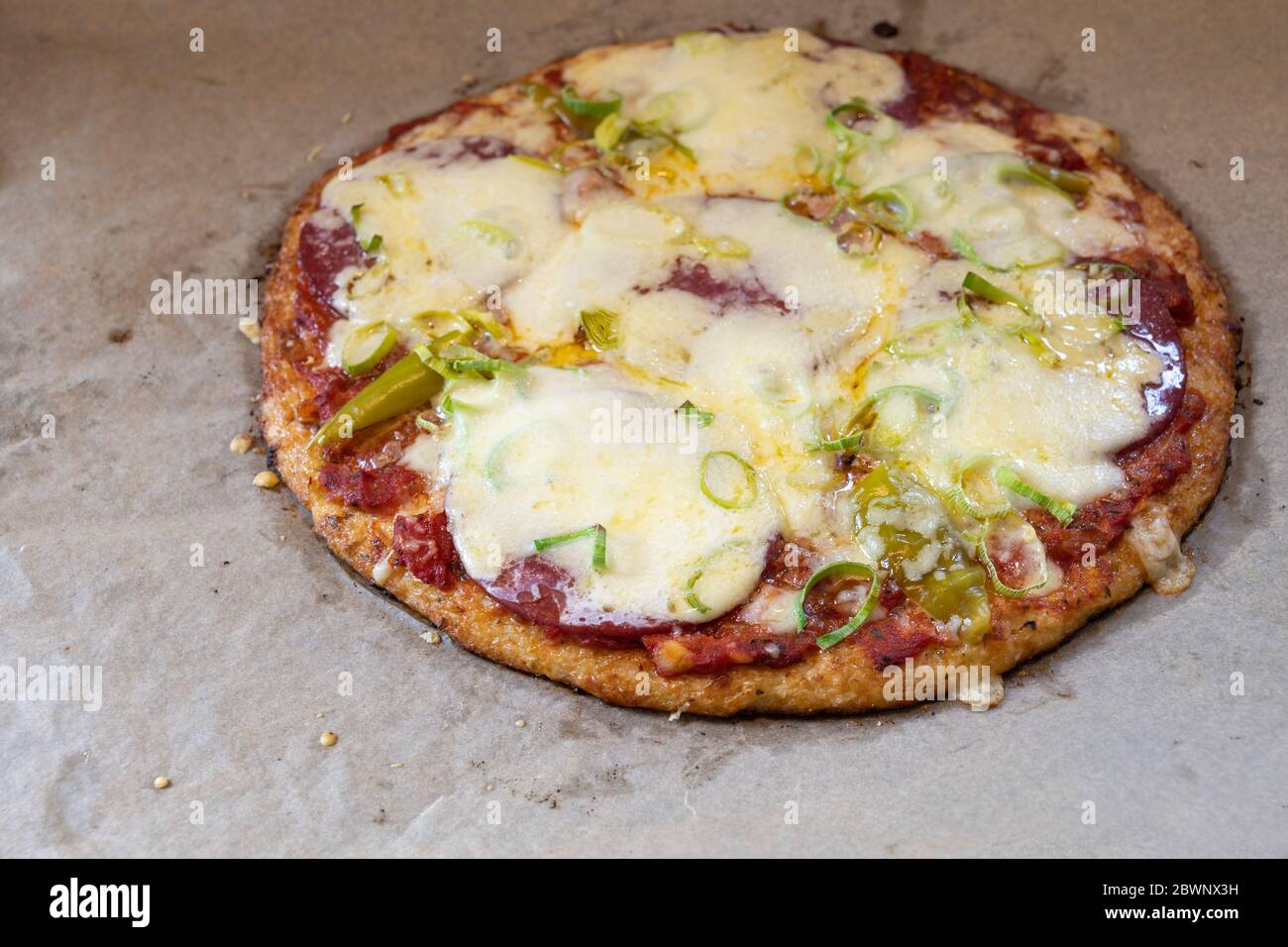 Pizza mit Blumenkohlenkruste mit Salami, Pepperoni, Lauch und Käse auf Backpapier, ausgewählter Fokus, schmale Schärfentiefe Stockfoto