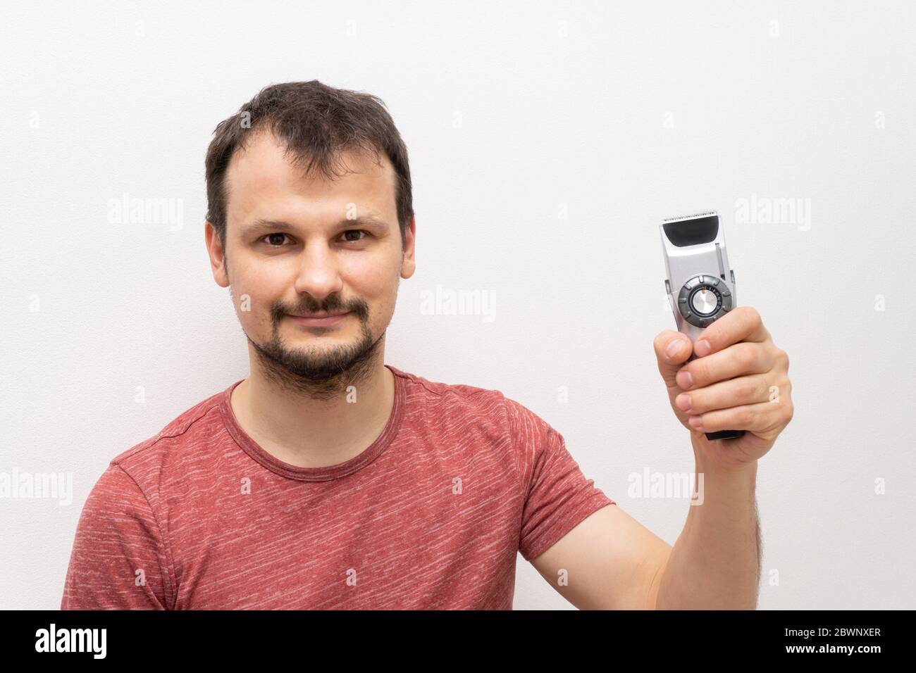 Kaukasischen Mann mit dunklen Haaren und Bart hält elektrische Rasierer, Stockfoto