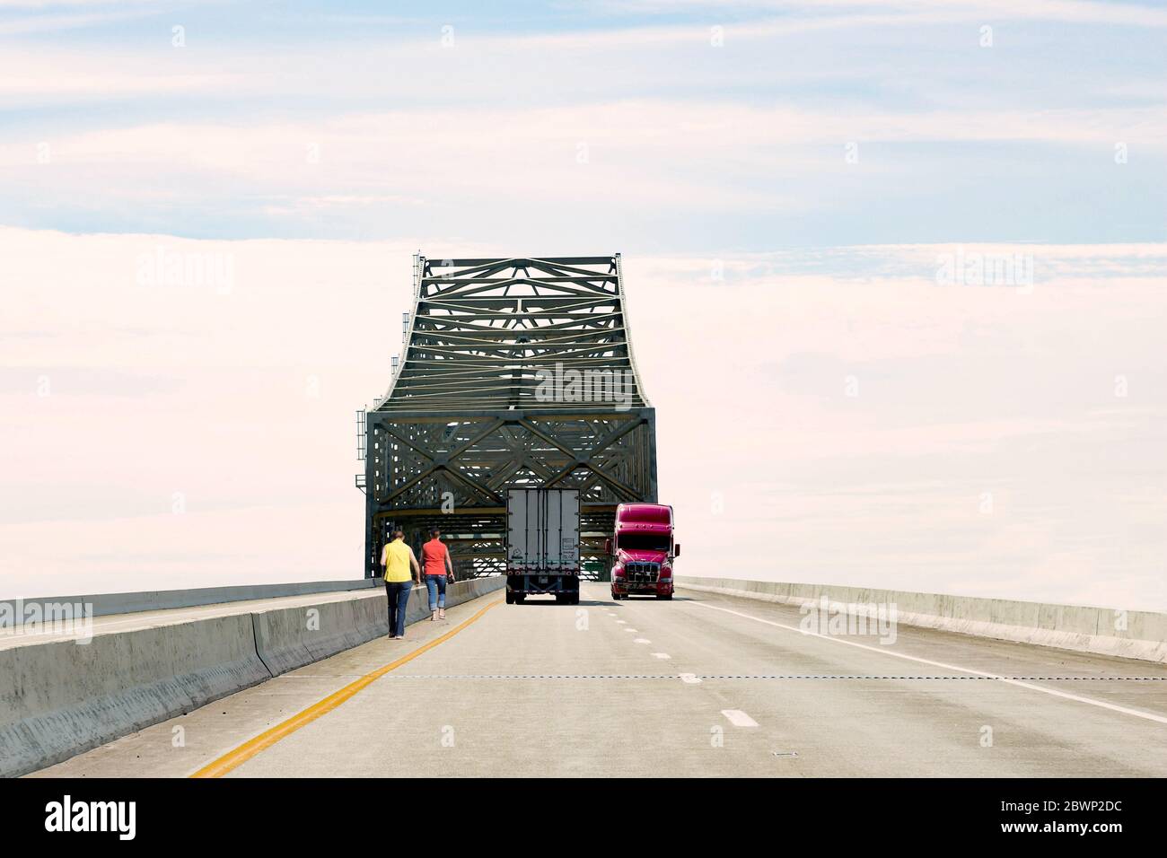 Zwei kaukasische Mann, der entlang der Seite der Autobahn unter einer hohen Betonbrücke mit Semi-Lastwagen mit hoher Geschwindigkeit. Stockfoto