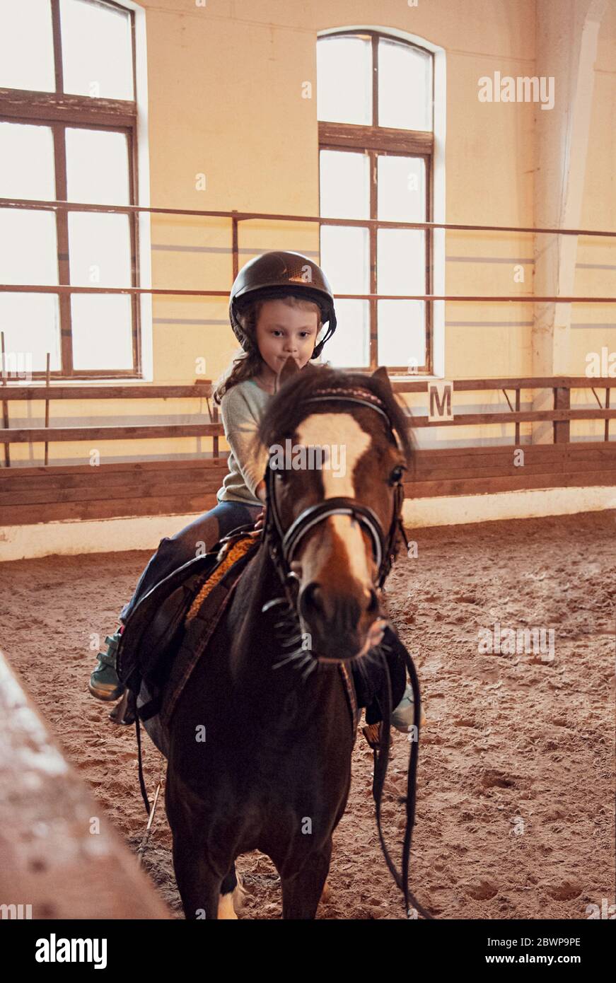 Nettes kleines Kind Mädchen lernen, ein Pferd in Bauernhof corral reiten. Hochformat Stockfoto