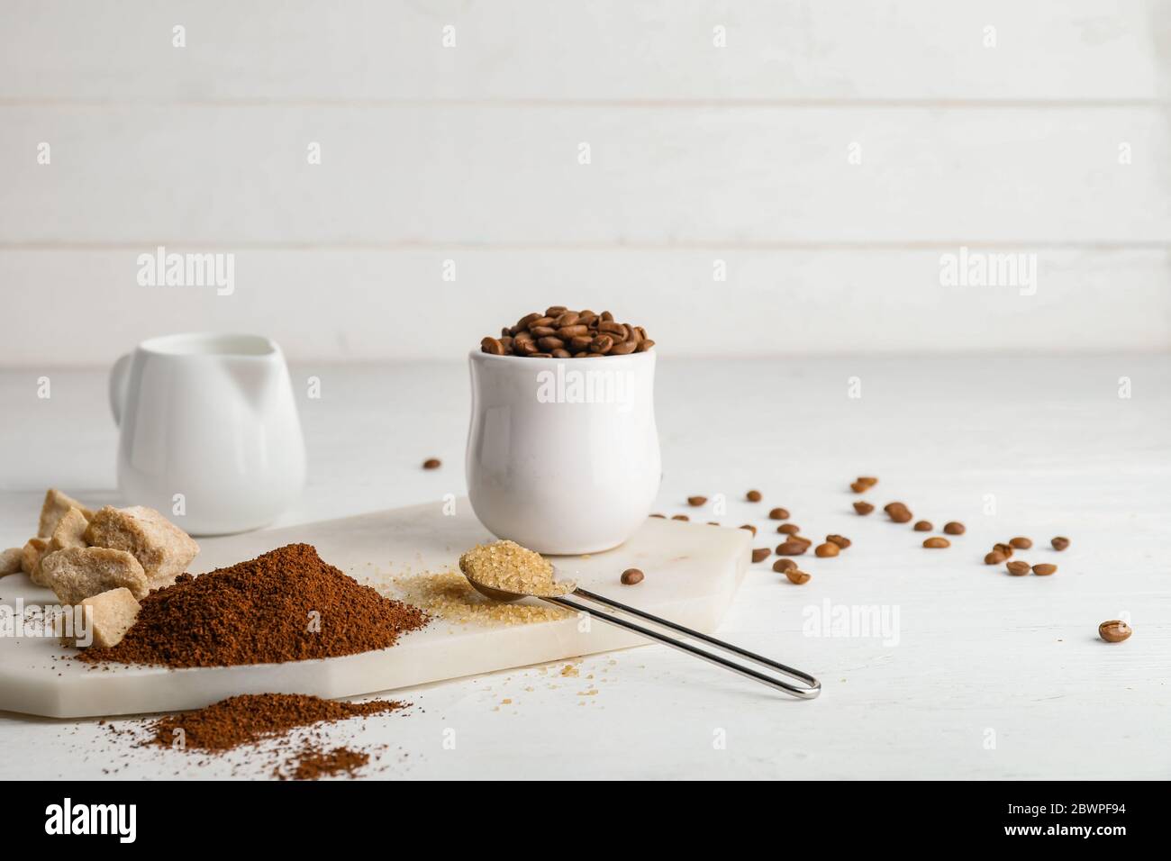Zusammensetzung mit Kaffeepulver, Bohnen, Zucker und Milch auf dem Tisch Stockfoto