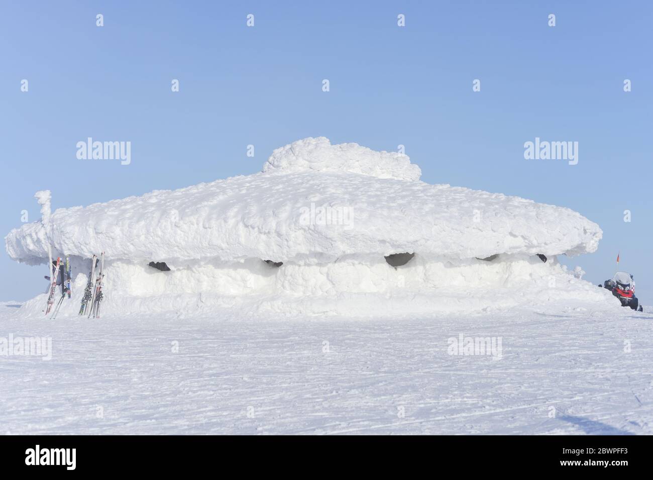 Im Sonnenlicht ist dieses große, tief liegende Gebäude mit einer sehr dicken Schicht aus hellem weißen Schnee bedeckt. Die Skier werden an einem Ende des Gebäudes ausgeruht Stockfoto