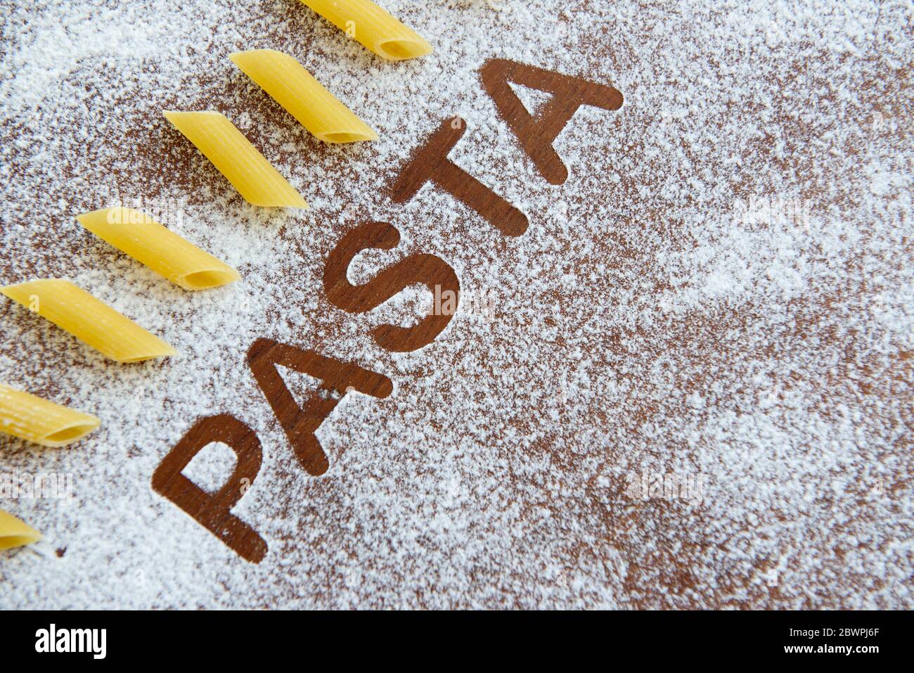 Holzhintergrund mit bestreut Mehl und das Wort Pasta geschrieben. Stockfoto