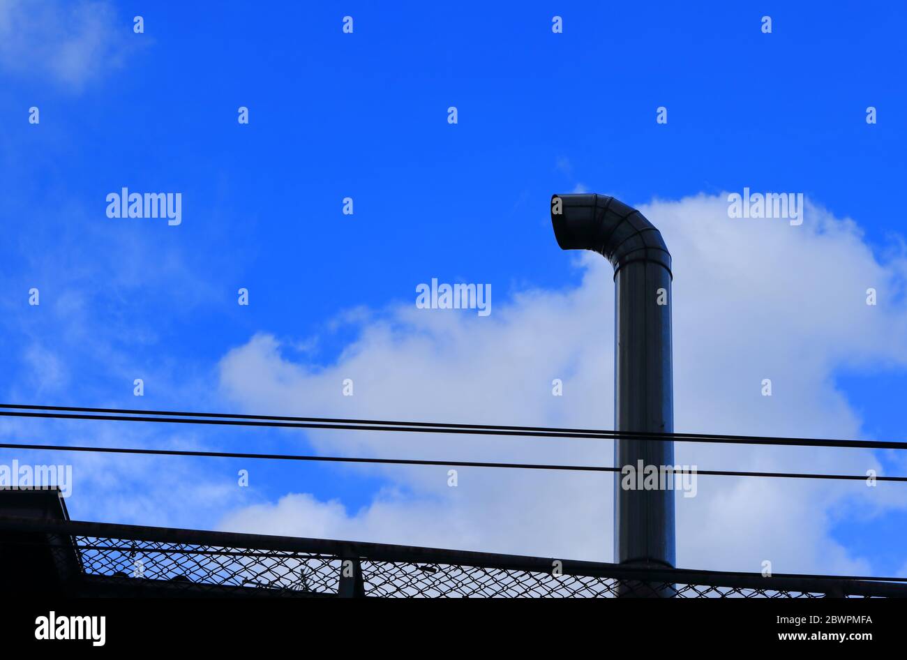 Closeup hohe Metall-Schornstein durch Schweißen verbunden, um eine Biegung nahe dem Ende der Öffnung zu machen, unter Sonnenlicht und Schatten, blauer Himmel mit weißen Wolke Stockfoto