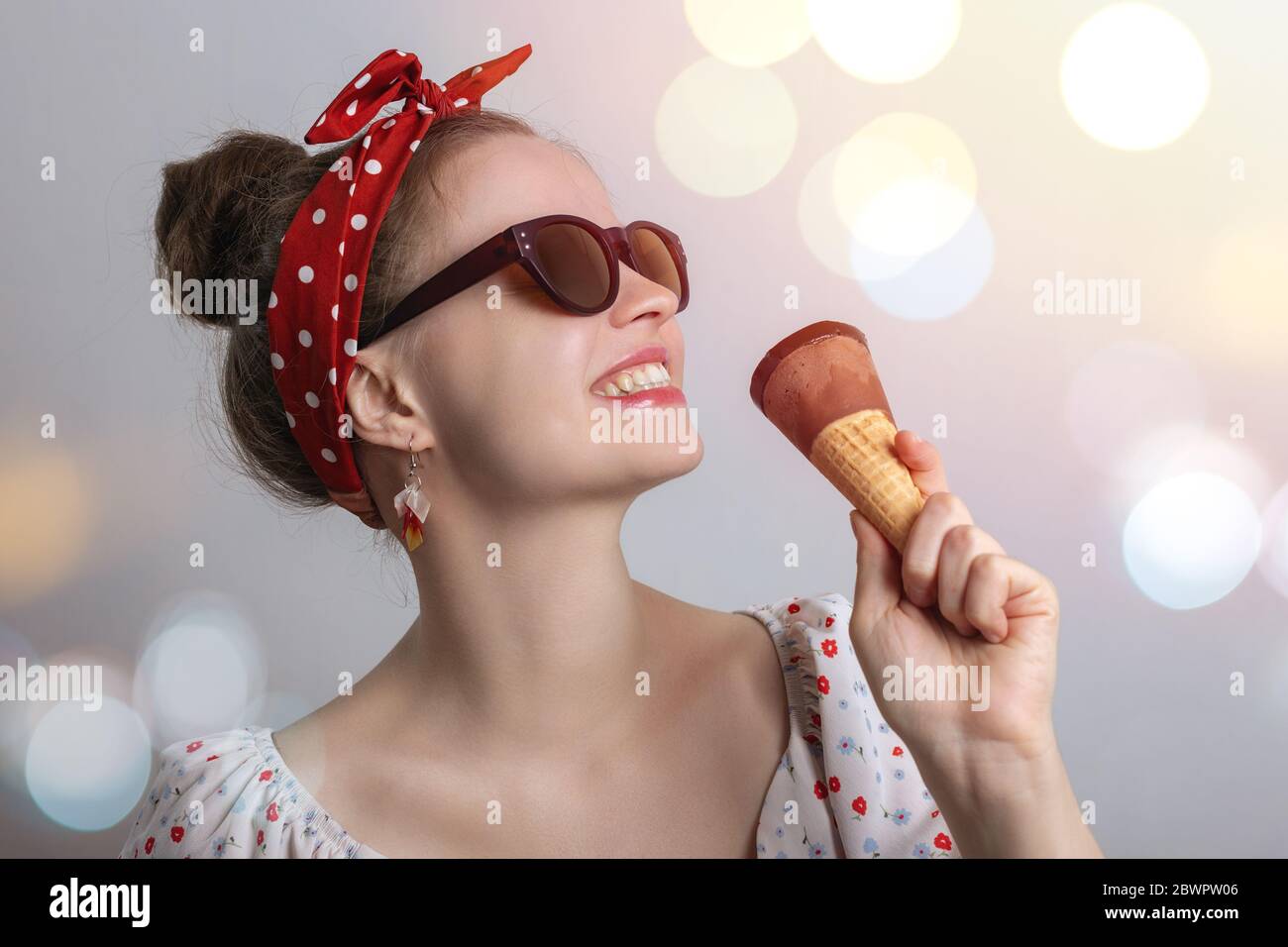Lächelnde junge kaukasische Frau Mädchen trägt Sonnenbrille essen eine Schokolade Eis-Kegel. Sommerparty Vibes Konzept Stockfoto