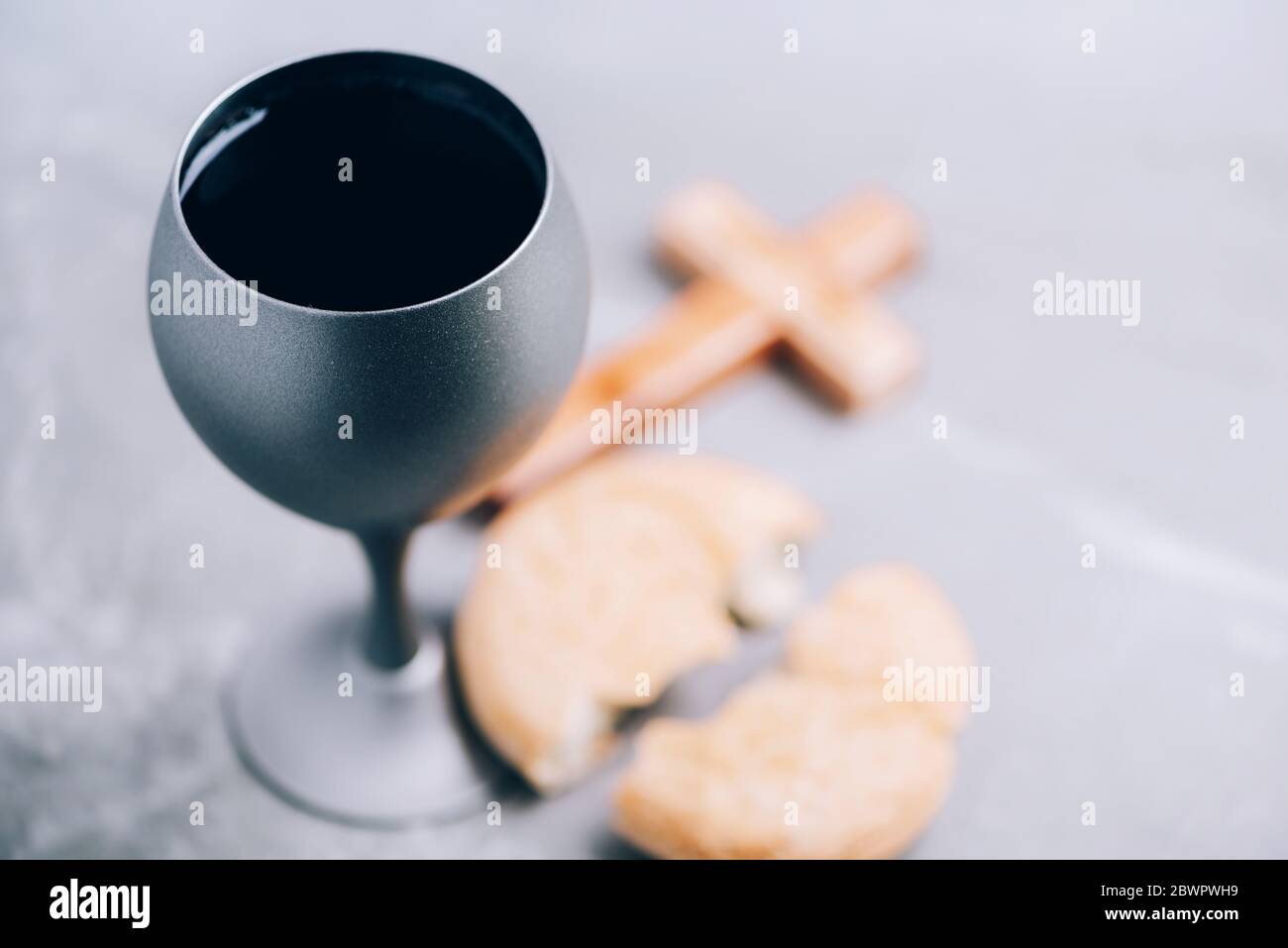 Ungesäuertes Brot, Kelch mit Wein, Holzkreuz auf grauem Hintergrund. Christliche Kommunion zur Erinnerung an das Opfer Jesu. Osterpassah. Eucharistie Stockfoto