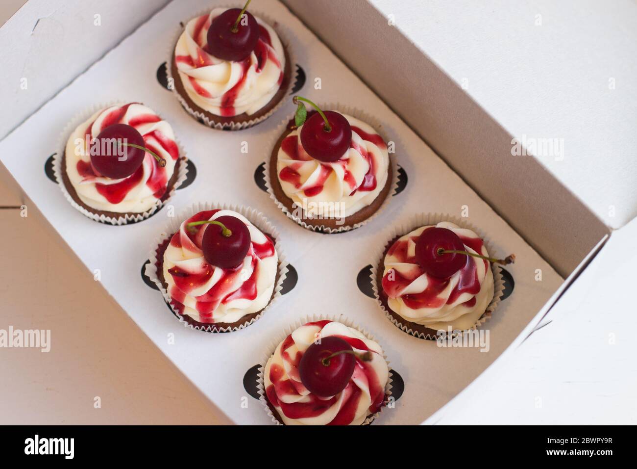 Vanillekuchen in Geschenkbox mit Beerensauce, Schlagsahne und frischen Kirschen auf der Oberseite. Selektiver Fokus. Stockfoto