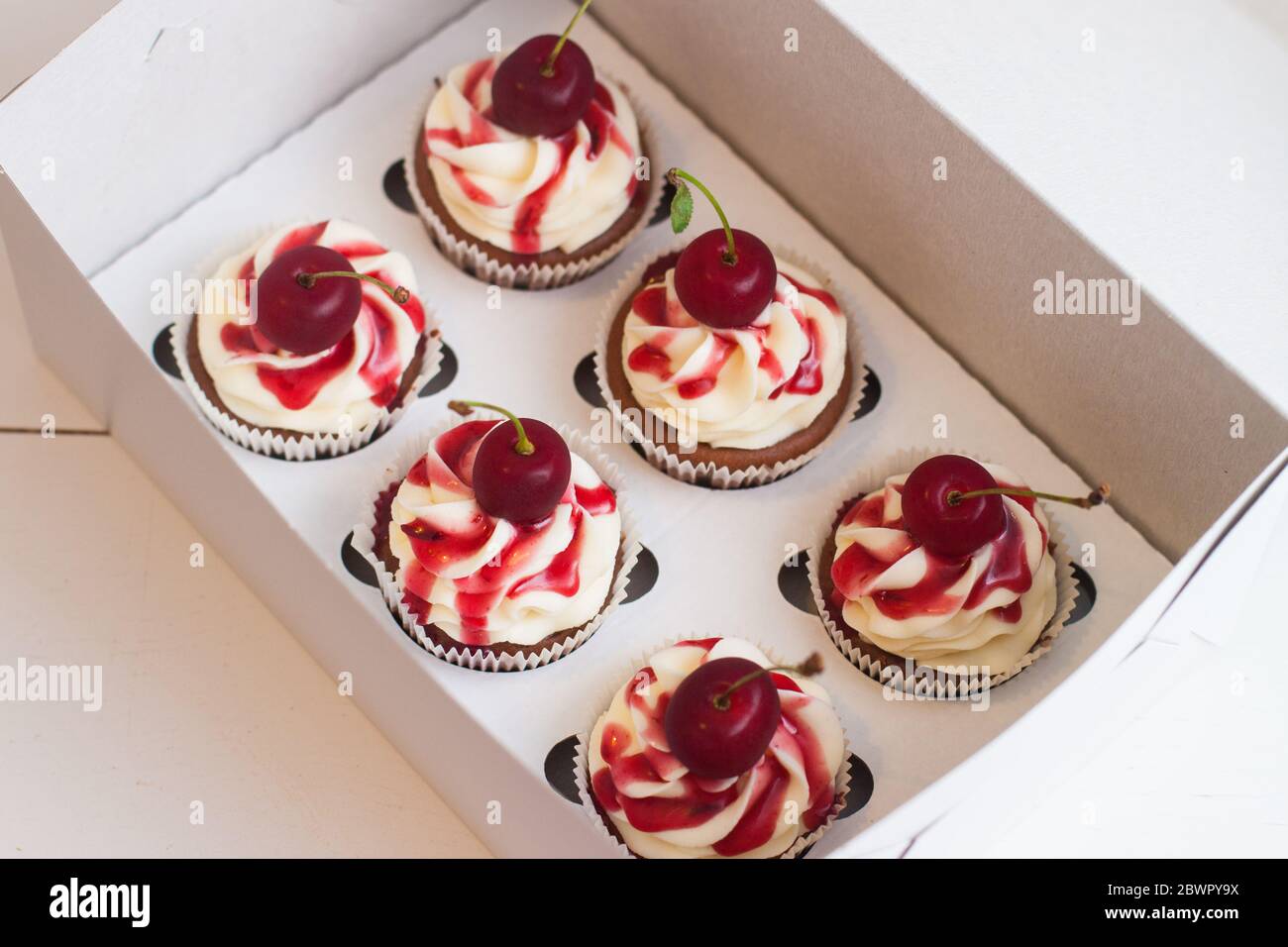 Vanillekuchen in Geschenkbox mit Beerensauce, Schlagsahne und frischen Kirschen auf der Oberseite. Selektiver Fokus. Stockfoto