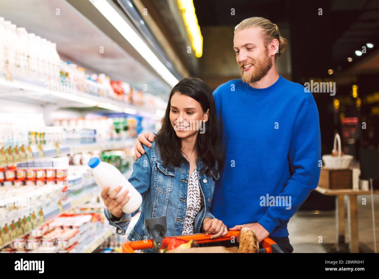 Junge lächelnde Paar mit Trolley voller Produkte glücklich die Wahl Milch im Supermarkt Stockfoto