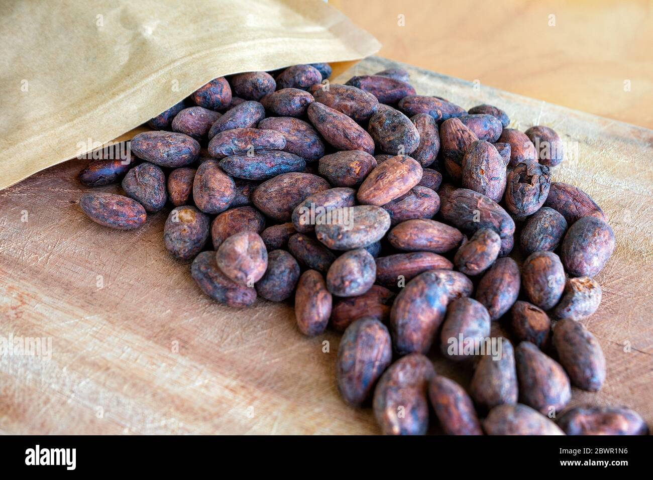Geröstete Kakaobohnen, die auf einem Holzhintergrund aus der Verpackung verschüttet wurden. Stockfoto