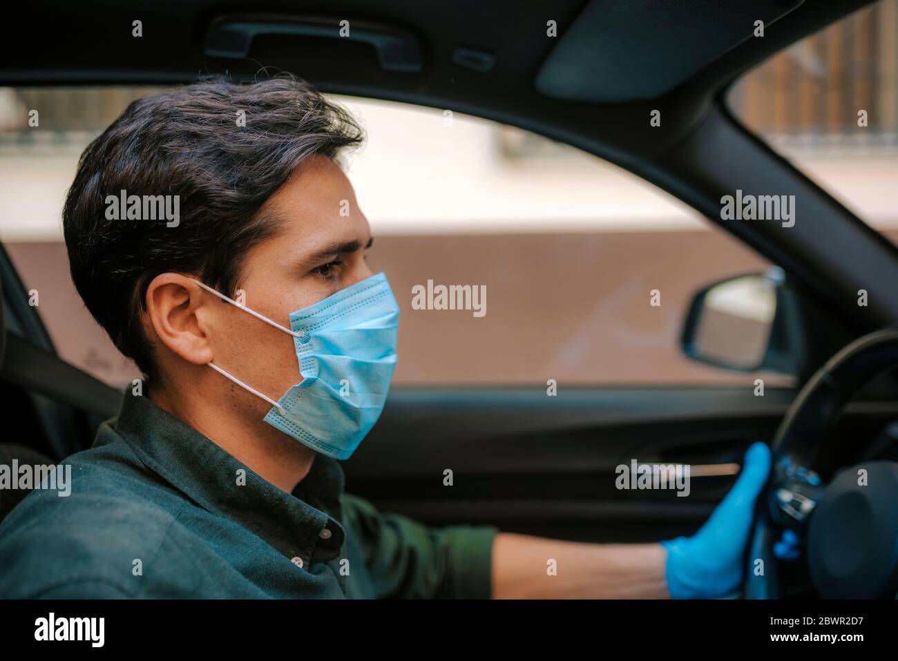 Ein Autofahrer legt während einer Epidemie eine medizinische Maske an, ein Taxifahrer in einer Maske, Schutz vor dem Virus. Fahrer im weißen Auto. Coronavirus, d Stockfoto
