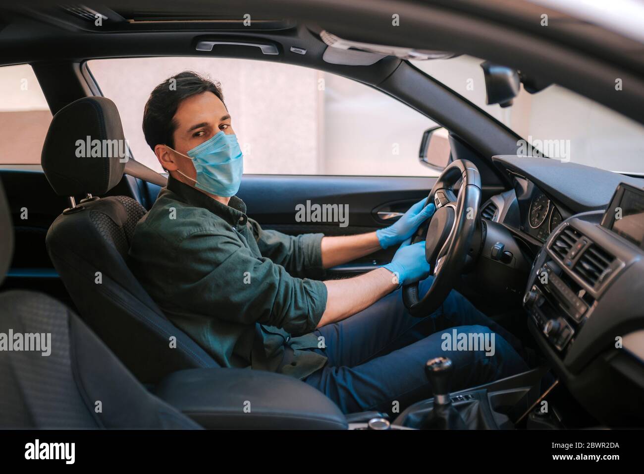 Ein Autofahrer legt während einer Epidemie eine medizinische Maske an, ein Taxifahrer in einer Maske, Schutz vor dem Virus. Fahrer im weißen Auto. Coronavirus, d Stockfoto