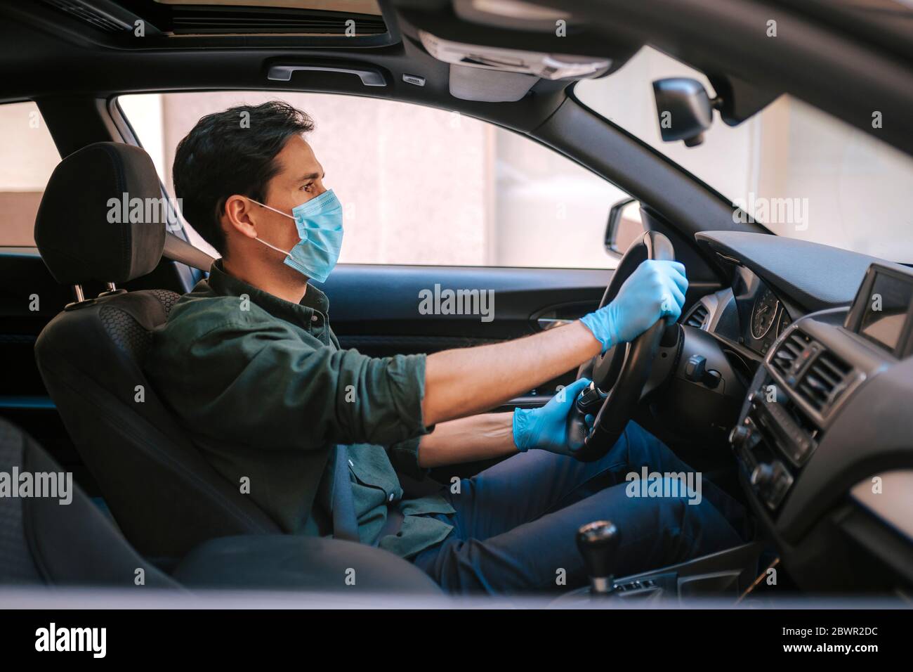 Ein Autofahrer legt während einer Epidemie eine medizinische Maske an, ein Taxifahrer in einer Maske, Schutz vor dem Virus. Fahrer im weißen Auto. Coronavirus, d Stockfoto