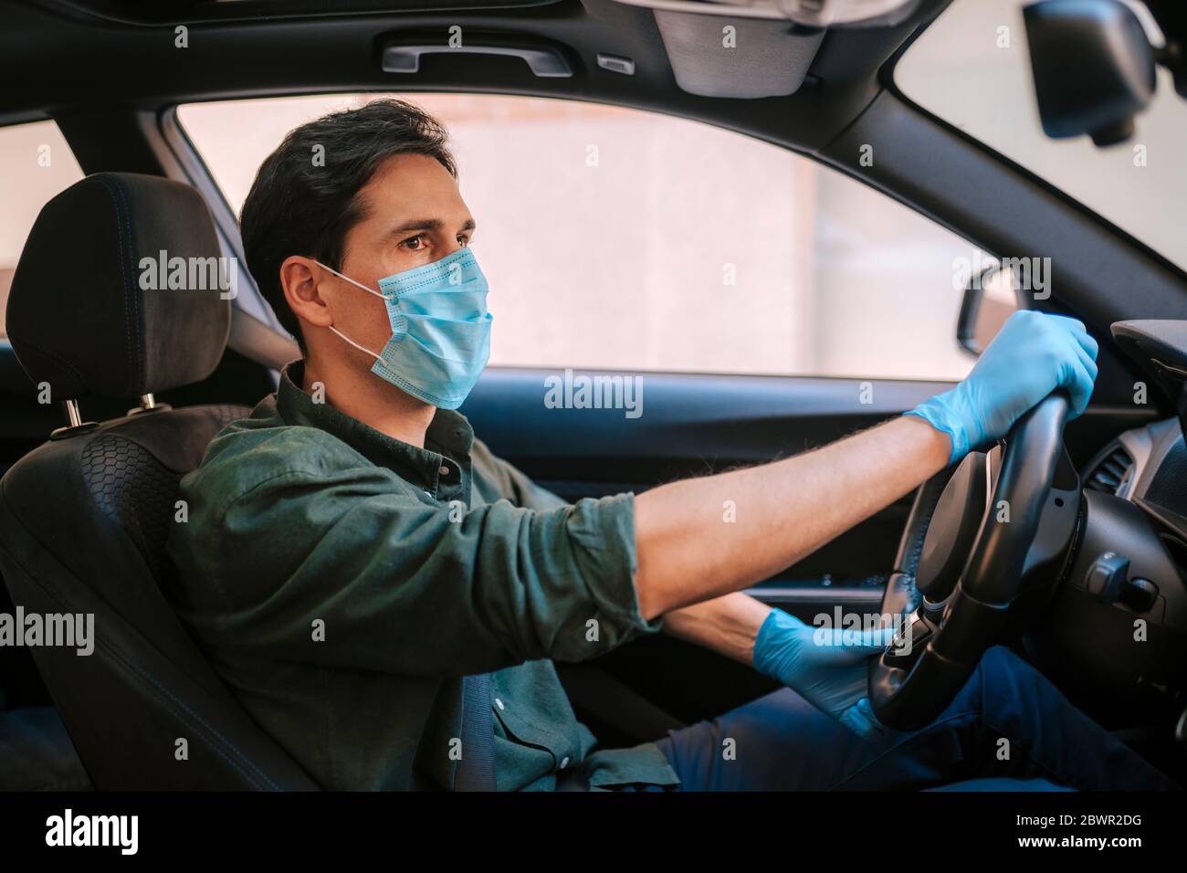 Ein Autofahrer legt während einer Epidemie eine medizinische Maske an, ein Taxifahrer in einer Maske, Schutz vor dem Virus. Fahrer im weißen Auto. Coronavirus, d Stockfoto
