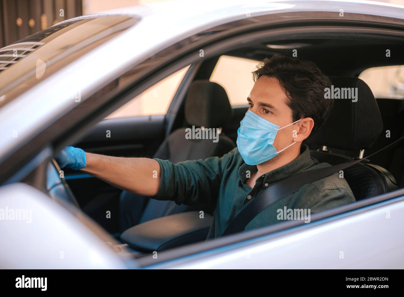 Ein Autofahrer legt während einer Epidemie eine medizinische Maske an, ein Taxifahrer in einer Maske, Schutz vor dem Virus. Fahrer im weißen Auto. Coronavirus, d Stockfoto