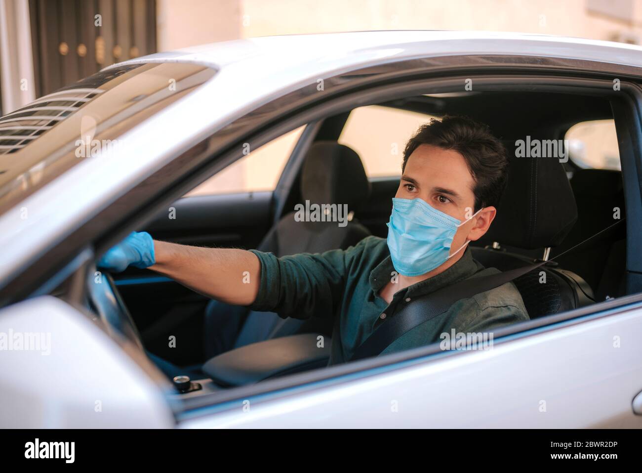 Ein Autofahrer legt während einer Epidemie eine medizinische Maske an, ein Taxifahrer in einer Maske, Schutz vor dem Virus. Fahrer im weißen Auto. Coronavirus, d Stockfoto