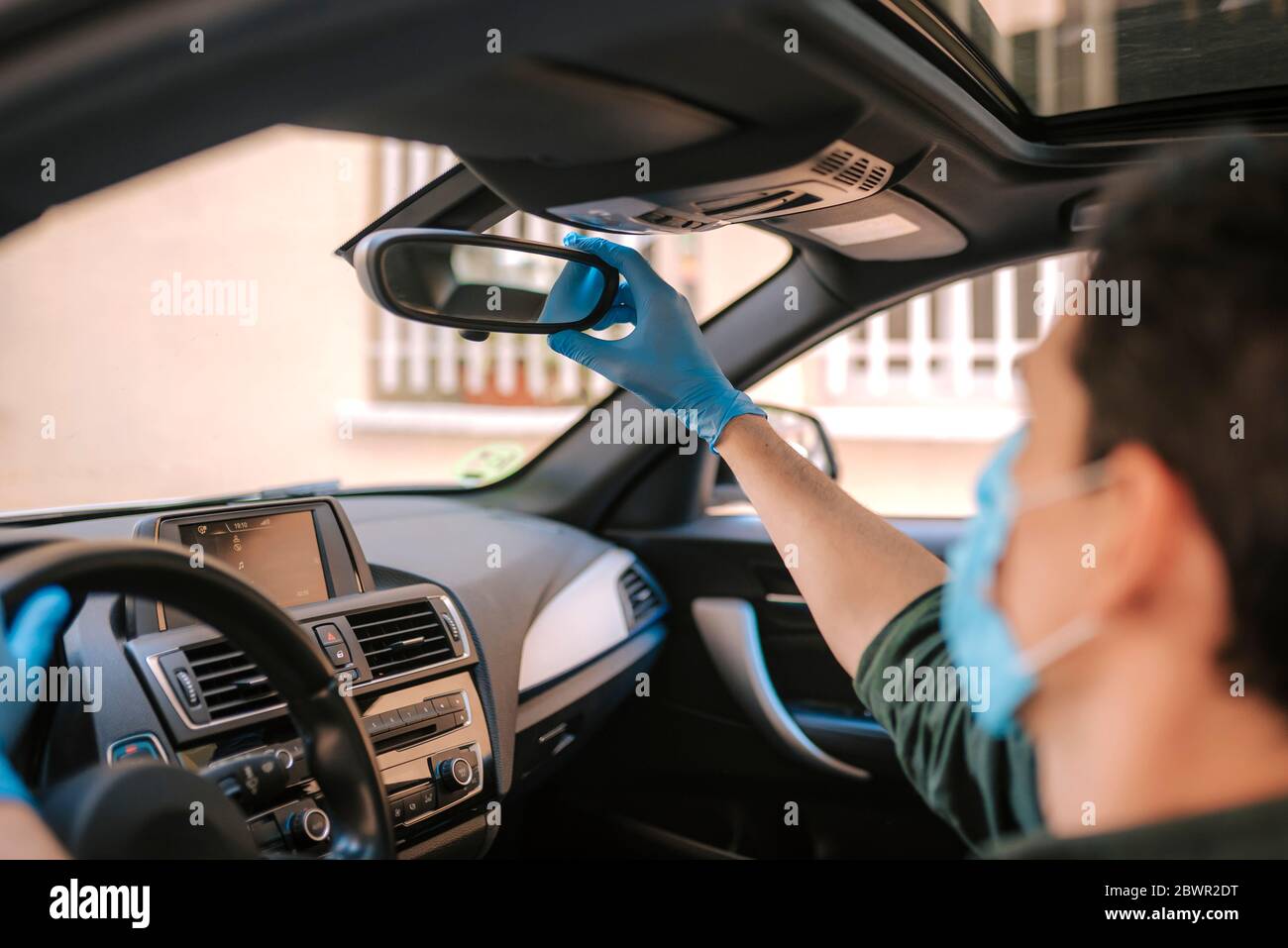 Ein Autofahrer legt während einer Epidemie eine medizinische Maske an, ein Taxifahrer in einer Maske, Schutz vor dem Virus. Fahrer im weißen Auto. Coronavirus, d Stockfoto