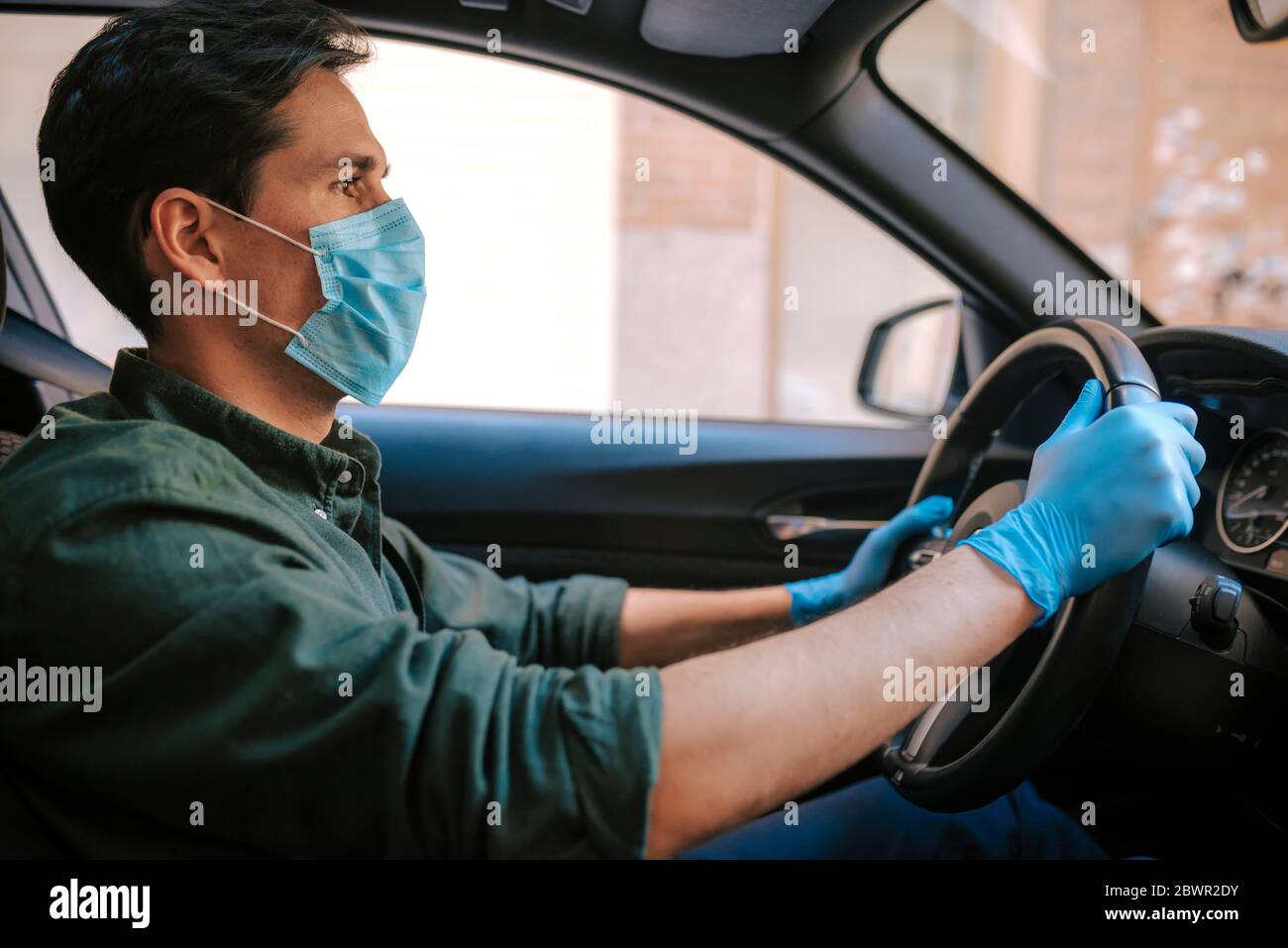 Ein Autofahrer legt während einer Epidemie eine medizinische Maske an, ein Taxifahrer in einer Maske, Schutz vor dem Virus. Fahrer im weißen Auto. Coronavirus, d Stockfoto