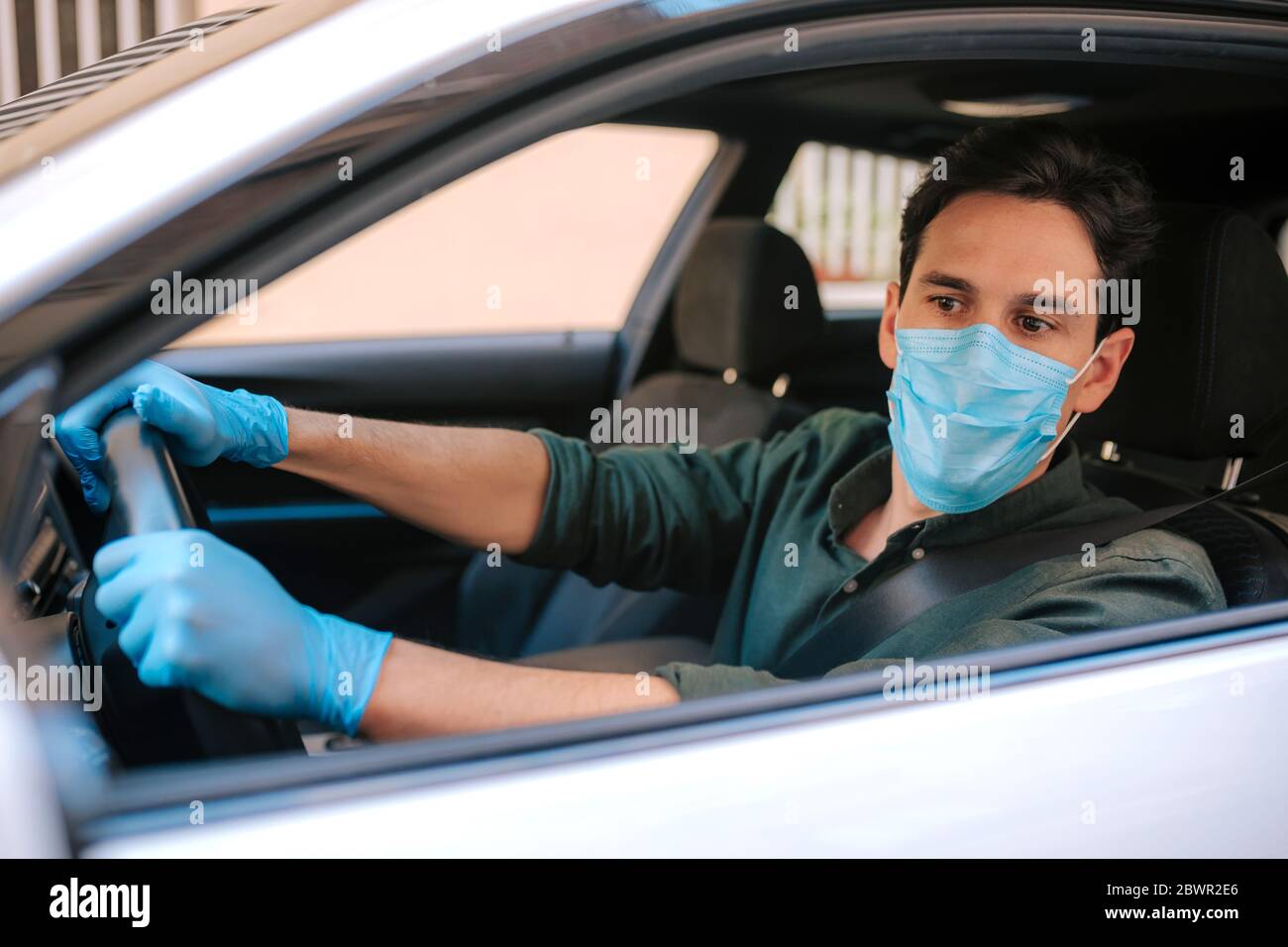 Ein Autofahrer legt während einer Epidemie eine medizinische Maske an, ein Taxifahrer in einer Maske, Schutz vor dem Virus. Fahrer im weißen Auto. Coronavirus, d Stockfoto