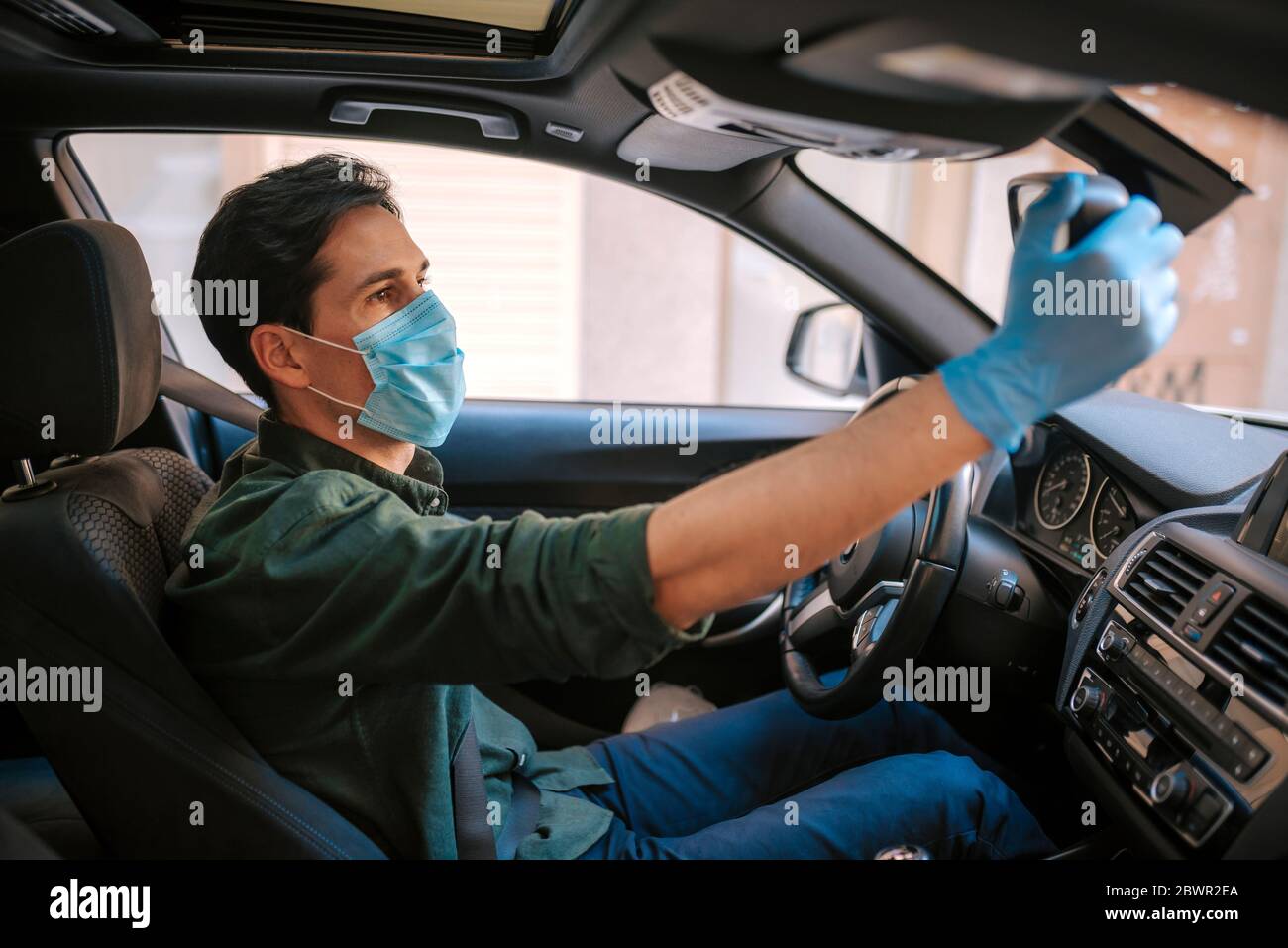 Ein Autofahrer legt während einer Epidemie eine medizinische Maske an, ein Taxifahrer in einer Maske, Schutz vor dem Virus. Fahrer im weißen Auto. Coronavirus, d Stockfoto