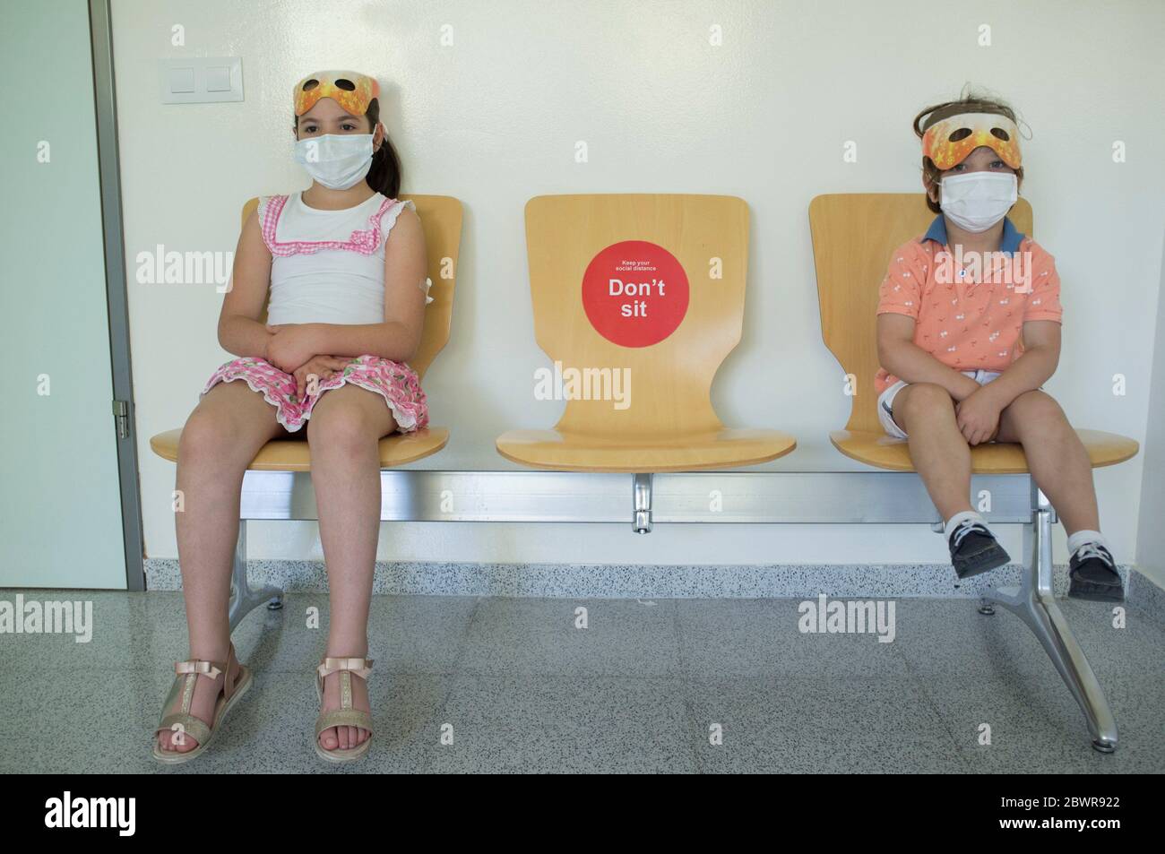 Kinder sitzen auf Wartestühlen mit sozialen Distanzaufkleber. Flur im Gesundheitszentrum. Stockfoto