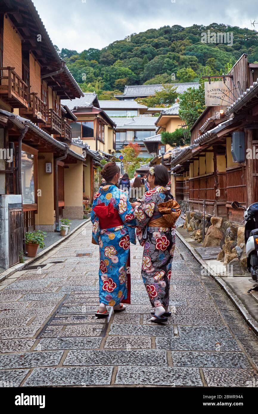 KYOTO, JAPAN - 18. OKTOBER 2019: Zwei junge japanische Mädchen im Kimono spazieren die Straße entlang zwischen den typischen Stadthäusern (Machiya) in der Mitte Stockfoto