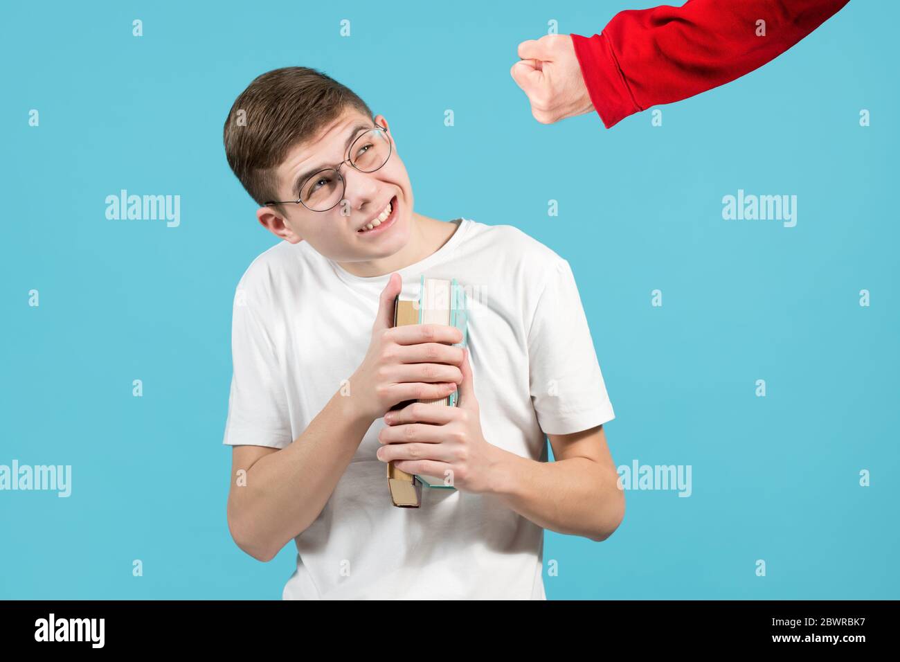 Die Faust eines Schlägerers in einem roten Sweatshirt bedroht einen Nerd Mit Brille und Buch Stockfoto