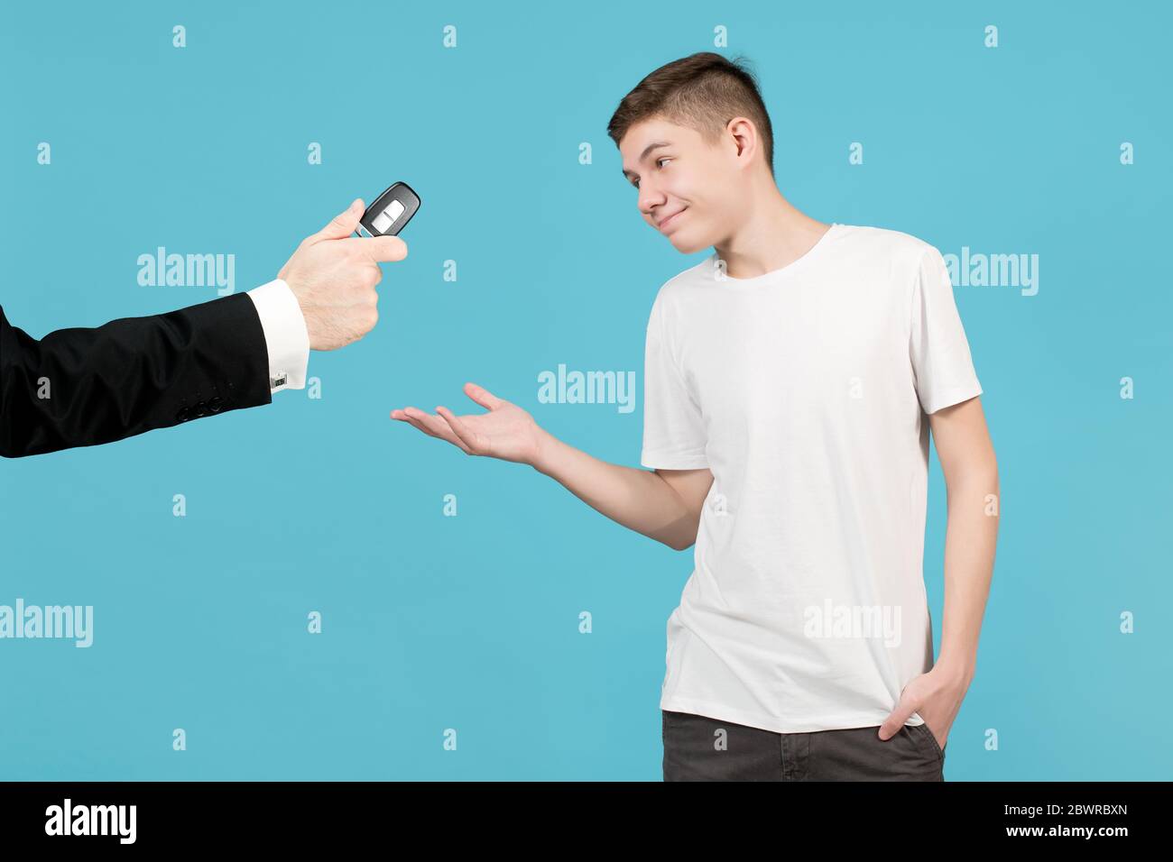 Ein Teenager nimmt glücklich einen Autoschlüssel an, den ihm ein Mann in einer Jacke aushält. Vielleicht erlaubt der Vater seinem Sohn, ein Auto zu fahren. Isoliert auf blau Stockfoto