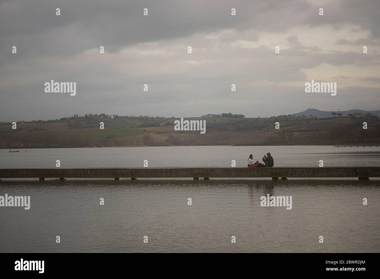 Junges Paar auf einem Pier des Sees Chiusi, von weitem gesehen, in Frieden getaucht Stockfoto