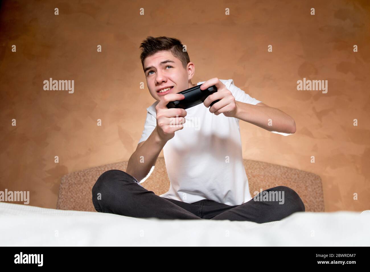 Ein Teenager ist in ein Spiel auf einer Spielkonsole involviert. ER verwendet einen modifizierten Joystick ohne Identifikationszeichen Stockfoto