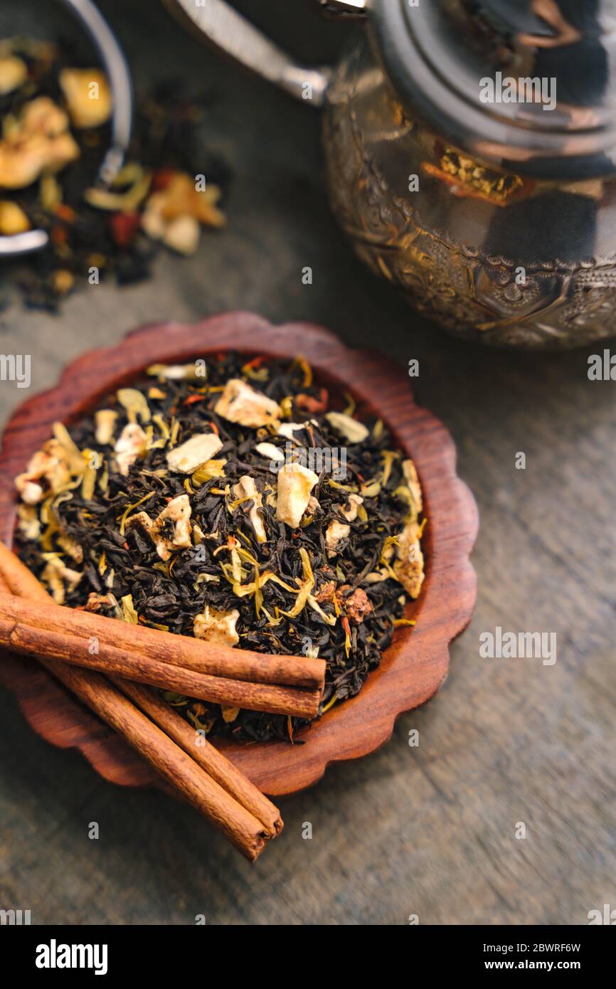 Aromatischer fruchtiger schwarzer Tee trockene Blätter auf kleinem Holztablett, Metallkessel und Zimtrindenstreifen auf einer Seite auf einer Holzfläche gesetzt Stockfoto