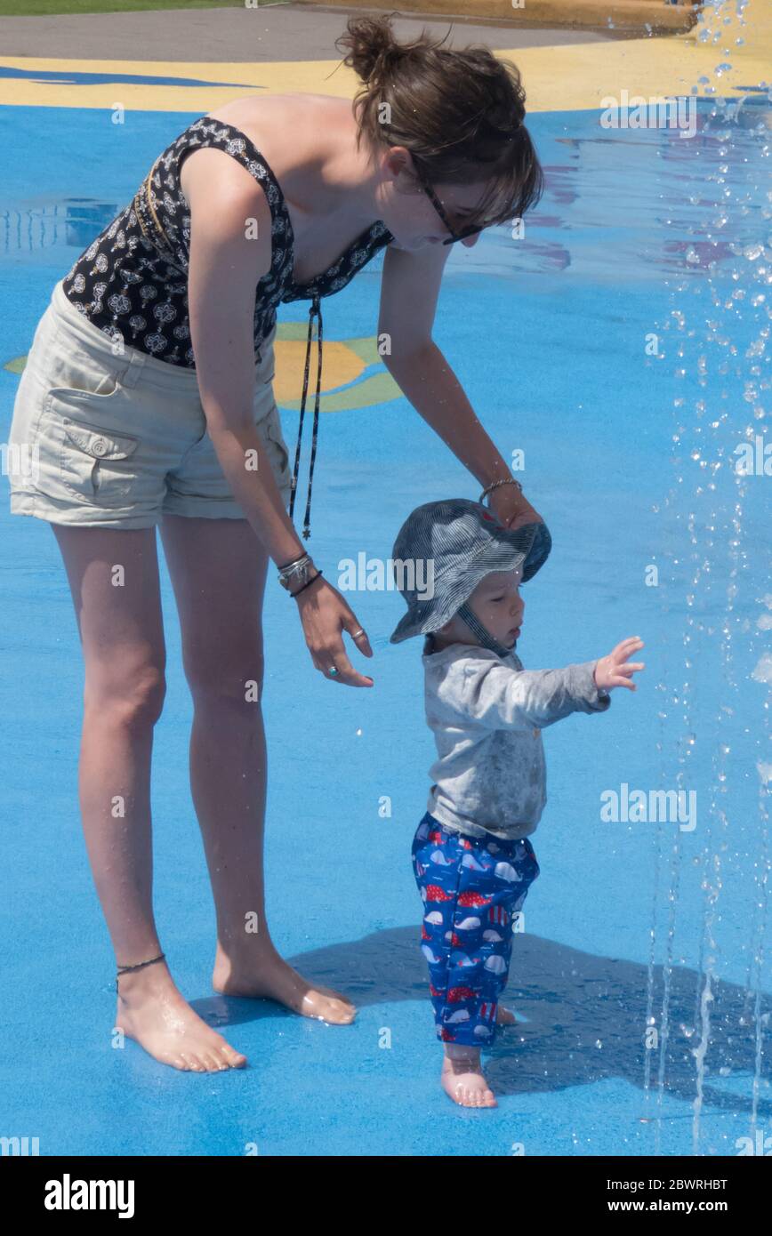 Junge Mutter und ihr Kleinkind Sohn, 8-9 Monate alt, spielen in einem Splash Park. MODELL FREIGEGEBEN Stockfoto