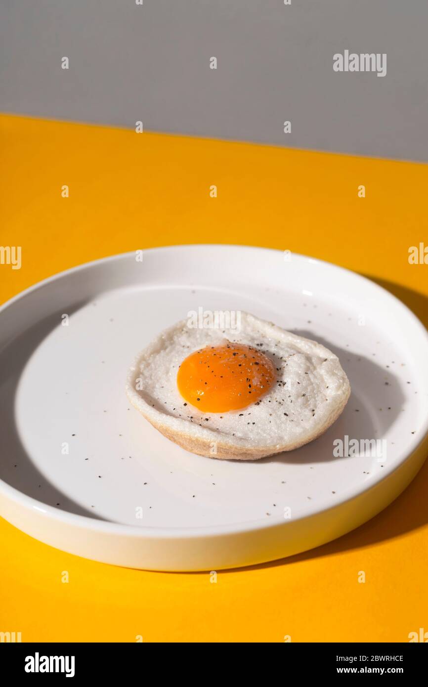 Spiegelei auf einem weißen Teller auf gelbem Hintergrund mit Schatten. Stockfoto