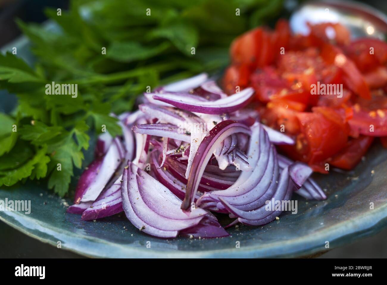 Rohzutaten für einen frischen Salat oder Wickelfüllung mit roten Zwiebeln, Tomaten und Kräutern, Nahaufnahme, ausgewählter Fokus und sehr schmaler Schärfentiefe Stockfoto