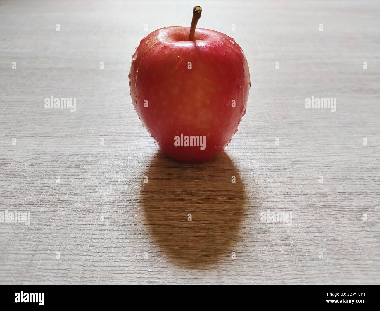 Einzelner roter Apfel mit Wassertropfen auf Holzhintergrund isoliert. Nahaufnahme von natürlichen Früchten Fotokonzept. Stockfoto