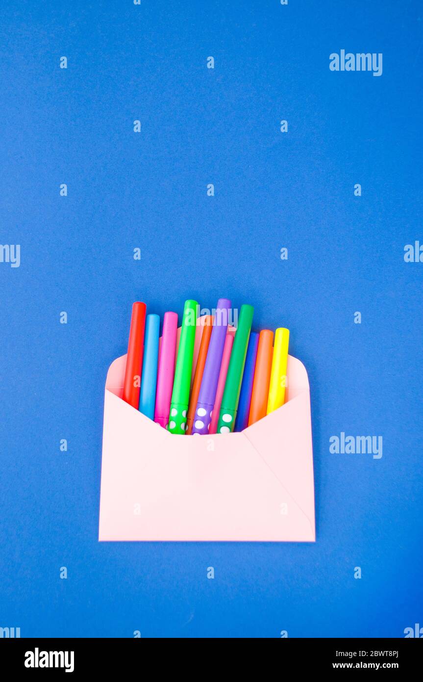 Papier rosa Umschlag mit bunten Markern innen auf klassisch blauen Hintergrund mit Copyspace. Stockfoto