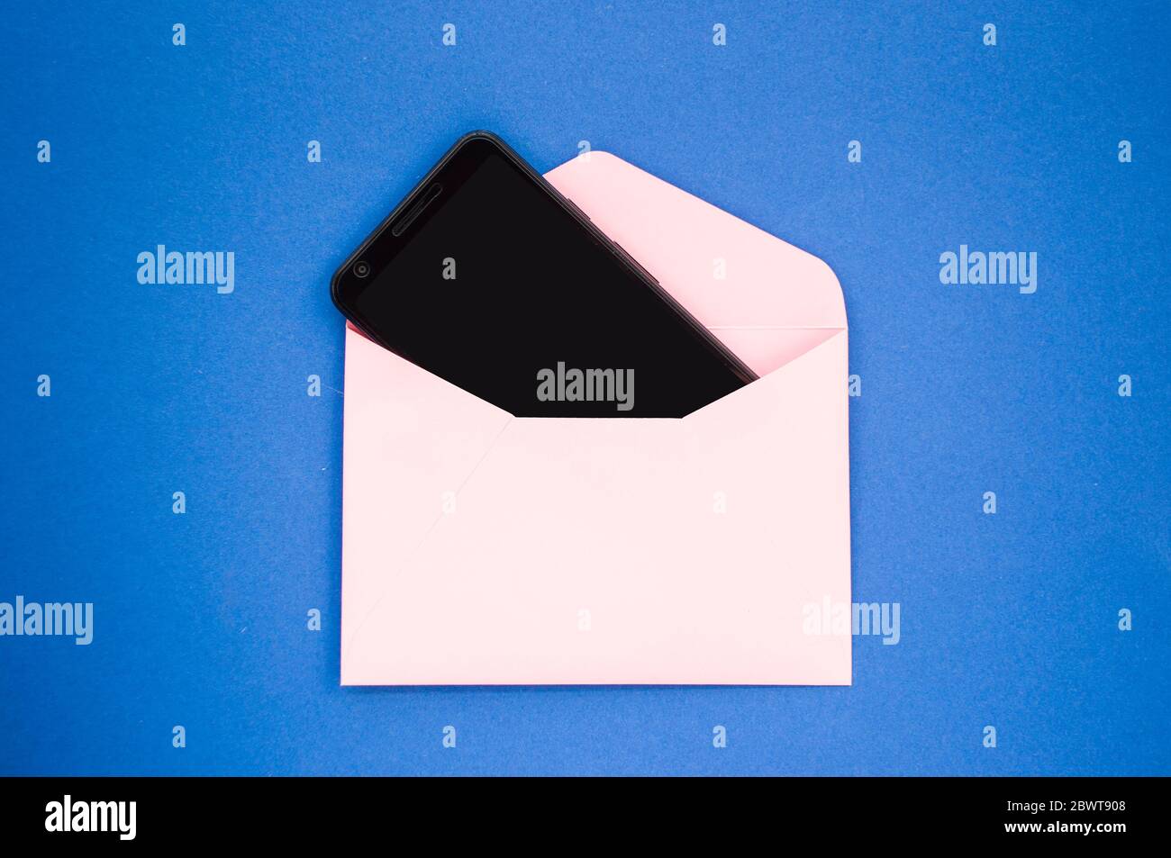 Papier rosa Umschlag mit schwarzem Smartphone innen auf klassischem blauen Hintergrund. Digitales Detox-Konzept. Stockfoto