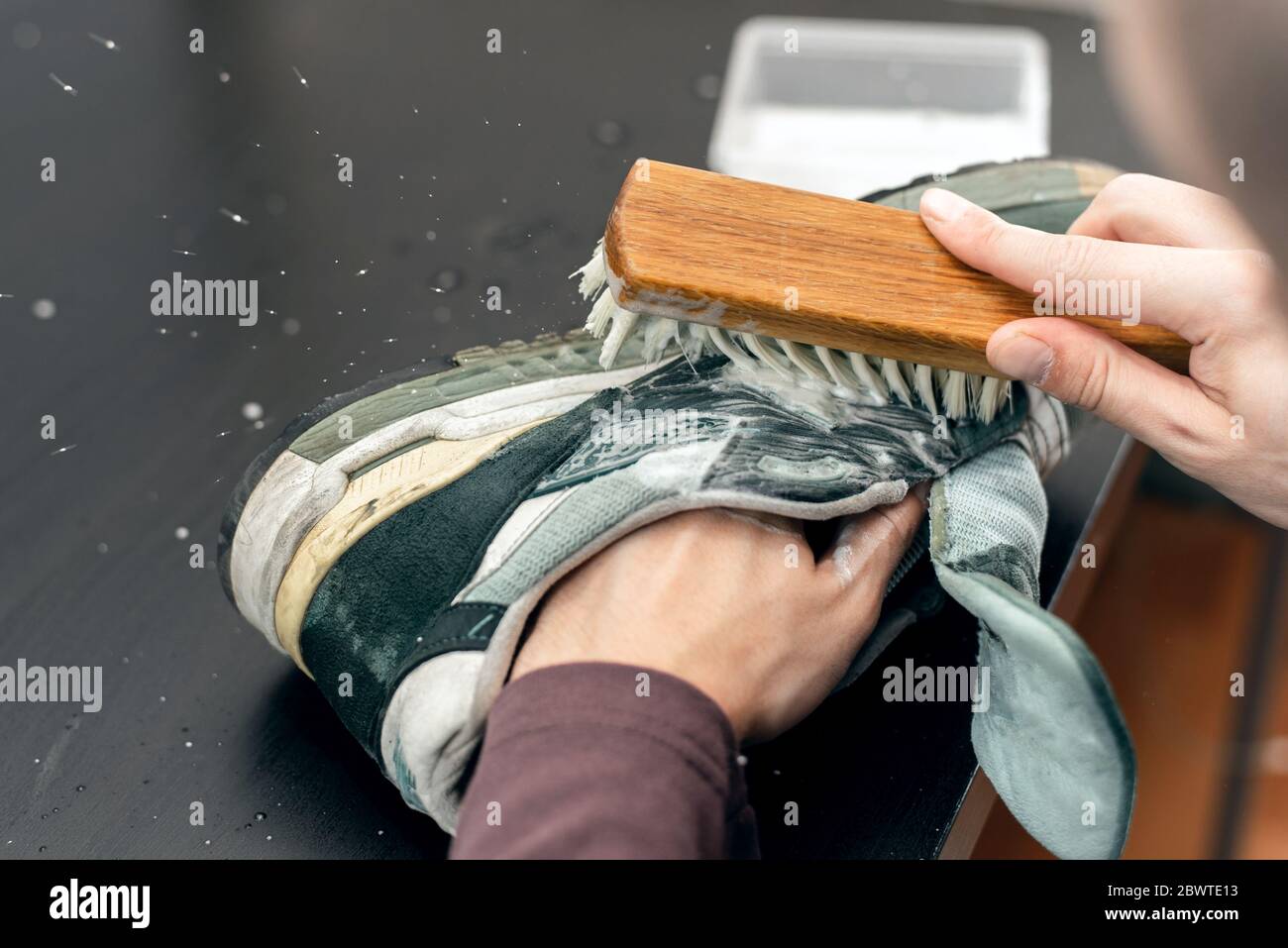Sneaker aus Wildleder. Ein Arbeiter in einer Schuhwerkstatt reinigt einen Haufen Schuhe. Stockfoto