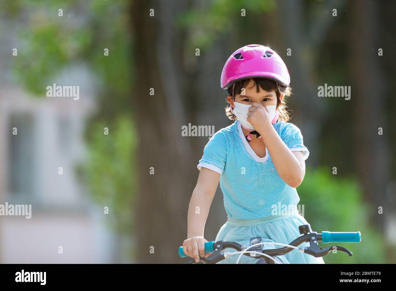 Kleines Mädchen in schützender medizinischer Maske fährt ein Fahrrad. Stockfoto