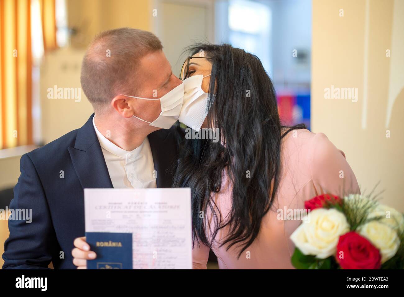 Galati, Rumänien - 10. April 2020: Verliebtes Paar gerade in einer Kovid-Pandemie verheiratet. Küssen mit Maske auf dem Gesicht und Hochzeitsurkunde in den Händen Stockfoto