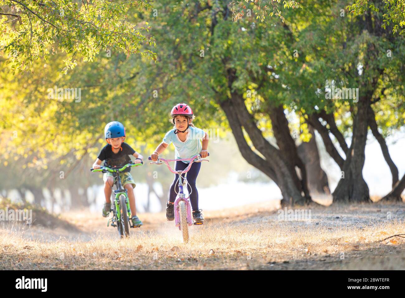 Glückliche Mädchen und Jungen Spaß im Herbst Park mit dem Fahrrad auf schönen Herbst Tag. Aktive Kinder Fahrrad Helm tragen Stockfoto