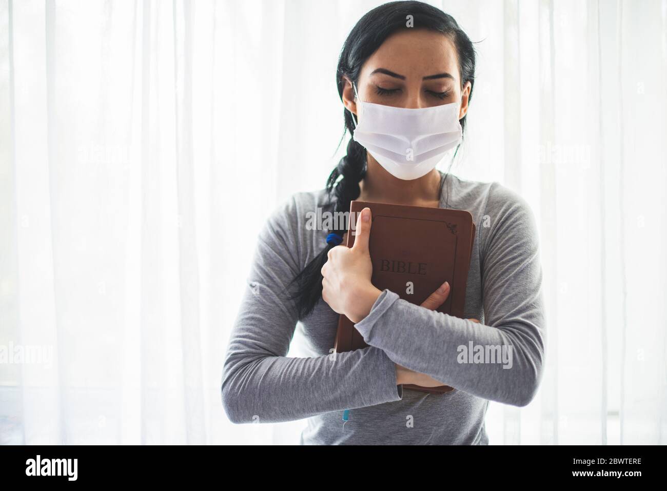 Porträt einer Frau mit einer chirurgischen Maske im Gesicht und einer bibel, die an ihrer Brust gehalten wird Stockfoto