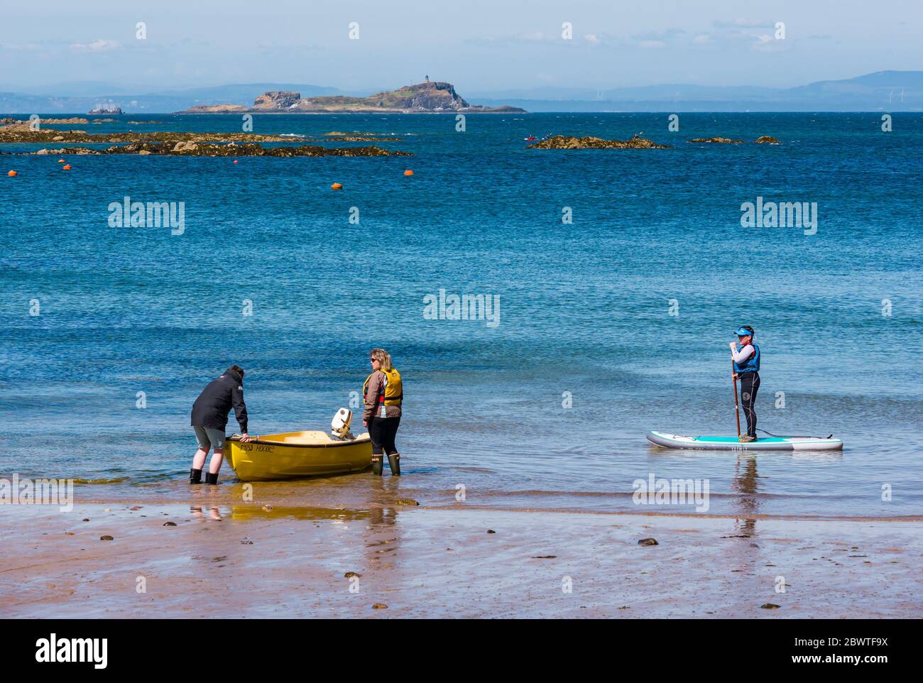Paddelboarding für Jungen und Paar, die ein kleines Boot ins Wasser bringen, mit Blick auf Fidra Island, North Berwick, East Lothian, Schottland, Großbritannien Stockfoto