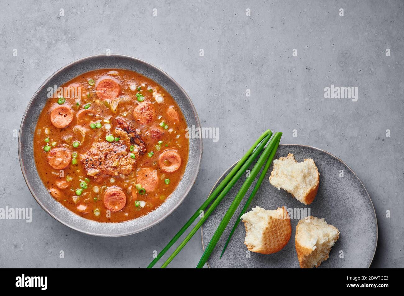 Hähnchen und Wurst Gumbo Suppe in grauen Schüssel auf Beton Hintergrund. Gumbo ist louisiana cajun Cuisine Suppe mit Roux. Amerikanische Küche in den USA. Traditionelle Ethnische Stockfoto